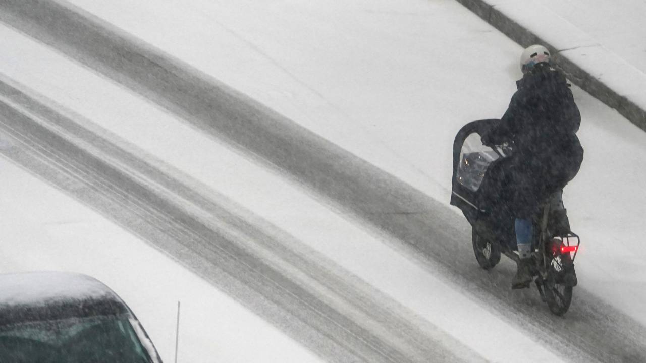 Eine Frau fährt mit einem Lastenfahrrad über eine verschneite Straße.
