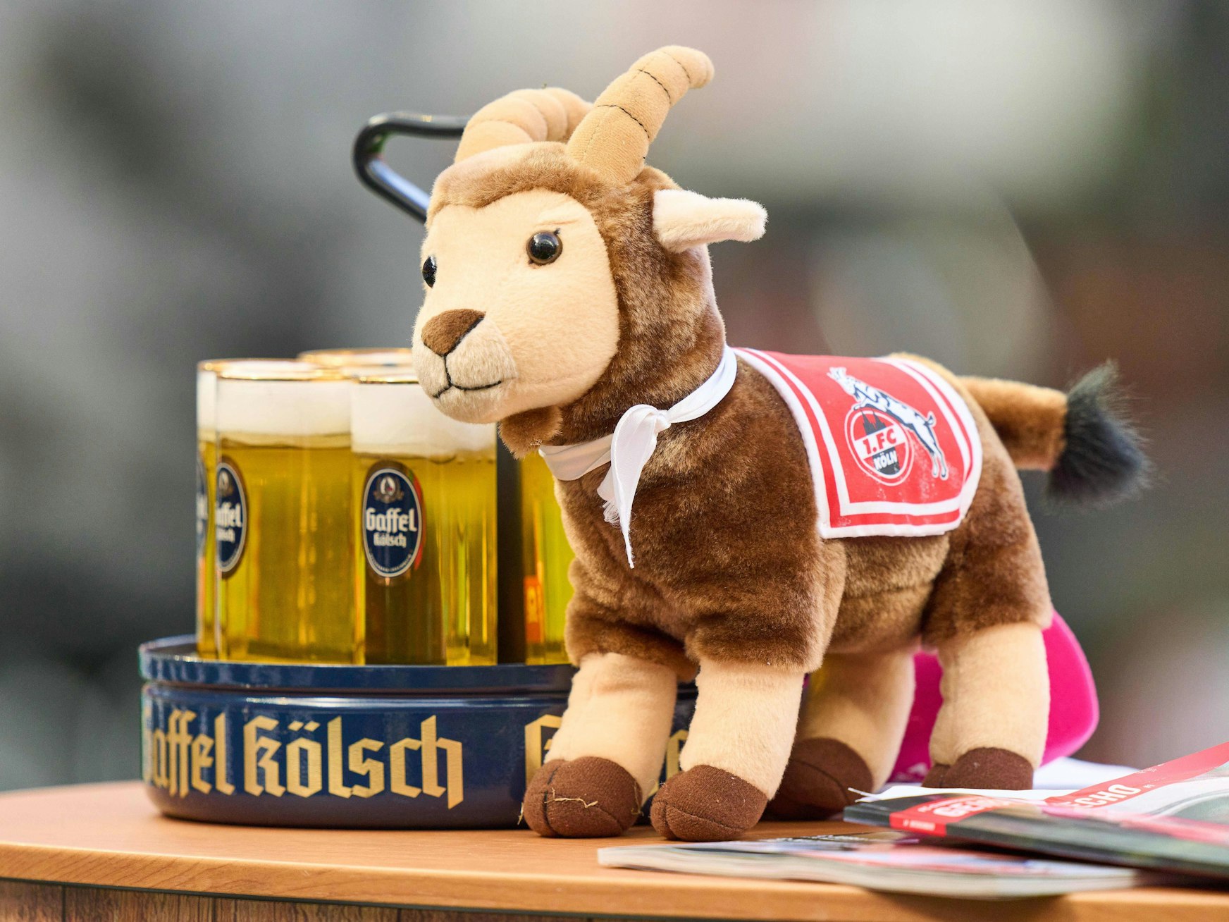 Ein Stofftier-Hennes steht neben einem Kölsch-Kranz im Rhein-Energie-Stadion.