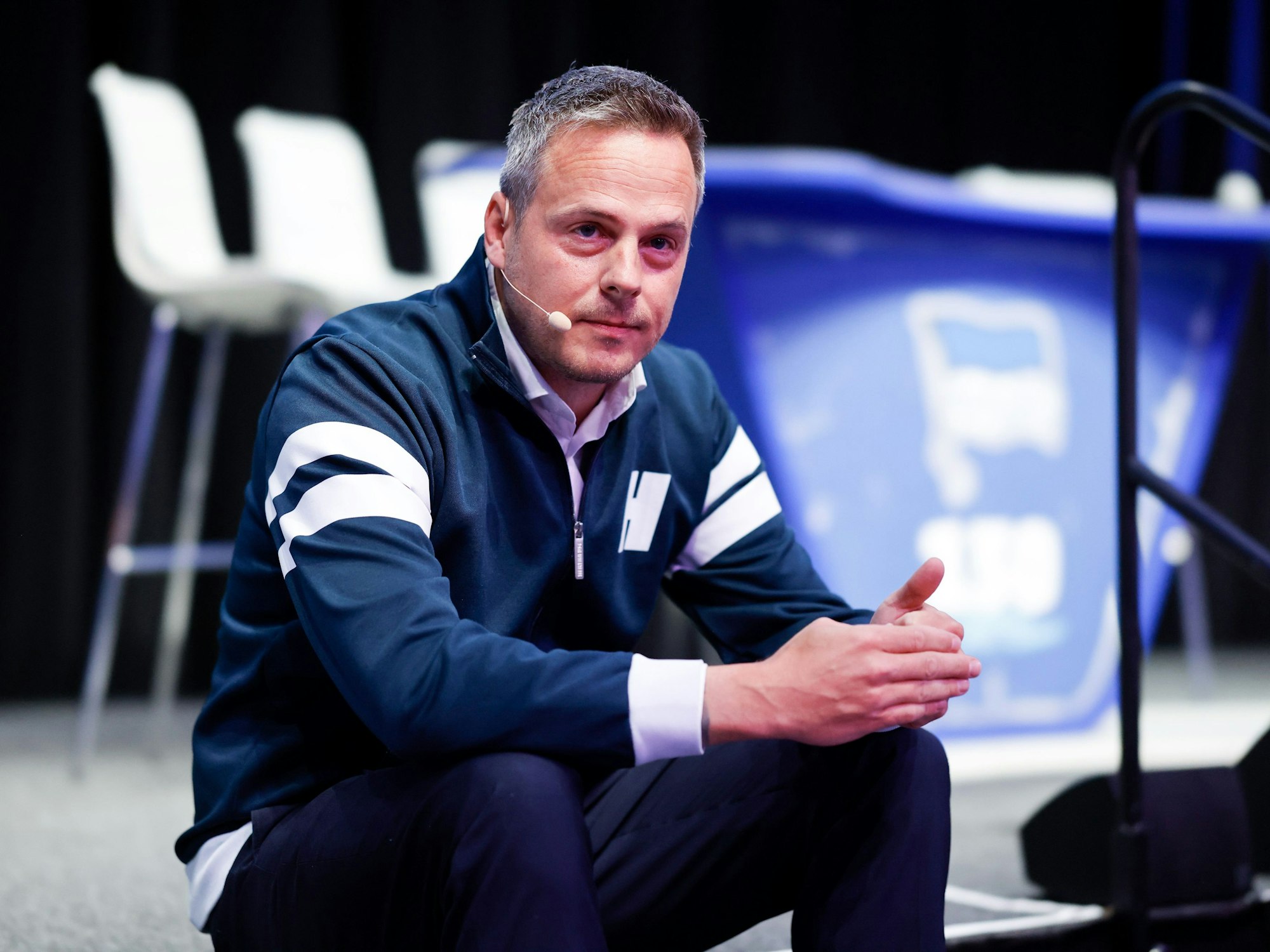 Herthas Präsident Kay Bernstein sitzt bei der Mitgliederversammlung in der Messe Berlin auf der Treppe zur Bühne.