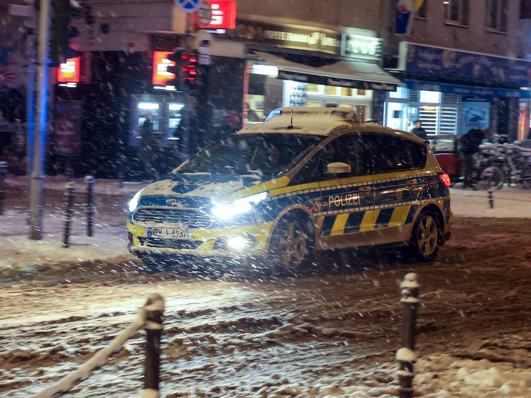 Ein Polizeiwagen fährt abends auf der Venloer Str. bei  Schneetreiben.
