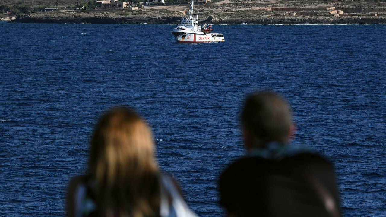Zwei Menschen auf einer Fähre schauen auf das Rettungsschiff „Open Arms“ der Hilfsorganisation Proactiva.