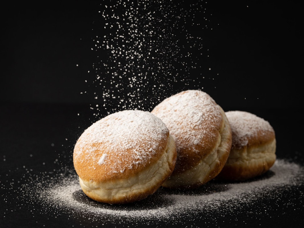 Drei Berliner, die mit Puderzucker verziert sind, liegen auf einem schwarzen Untergrund