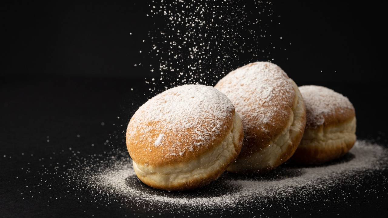 Drei Berliner, die mit Puderzucker verziert sind, liegen auf einem schwarzen Untergrund