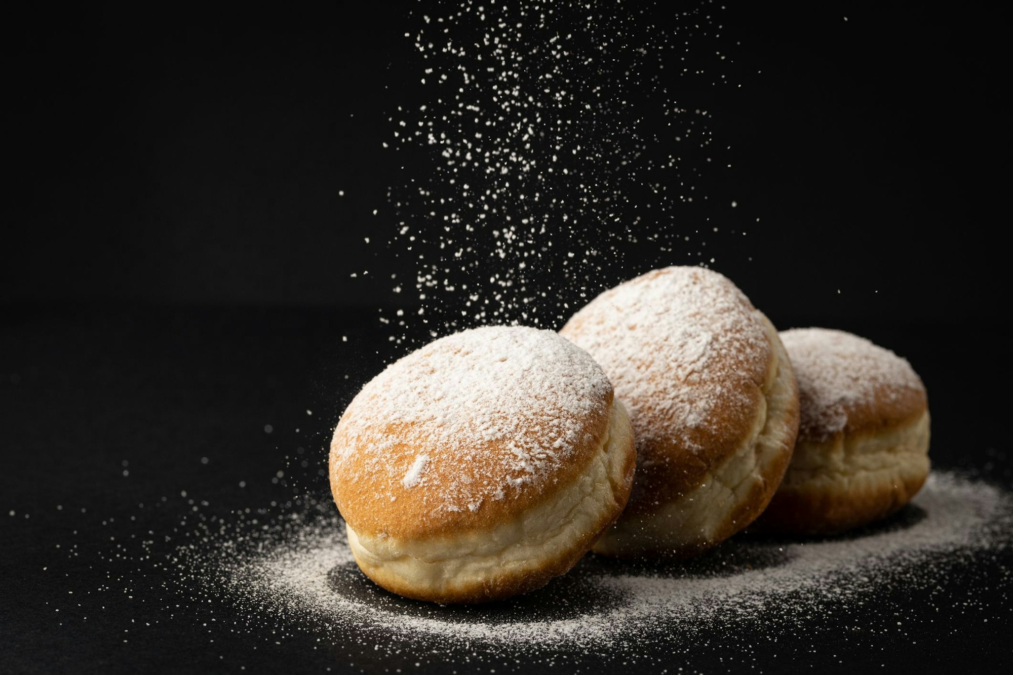 Drei Berliner, die mit Puderzucker verziert sind, liegen auf einem schwarzen Untergrund