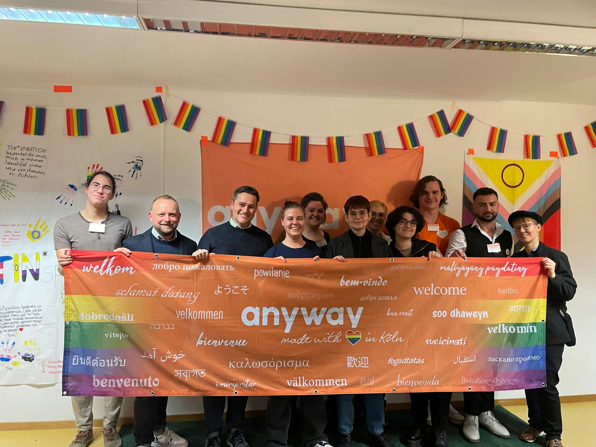 Mitarbeiterinnen und Mitarbeiter halten eine „anyway" Flagge und wünschen damit alle auf verschiedenen Sprachen willkommen.