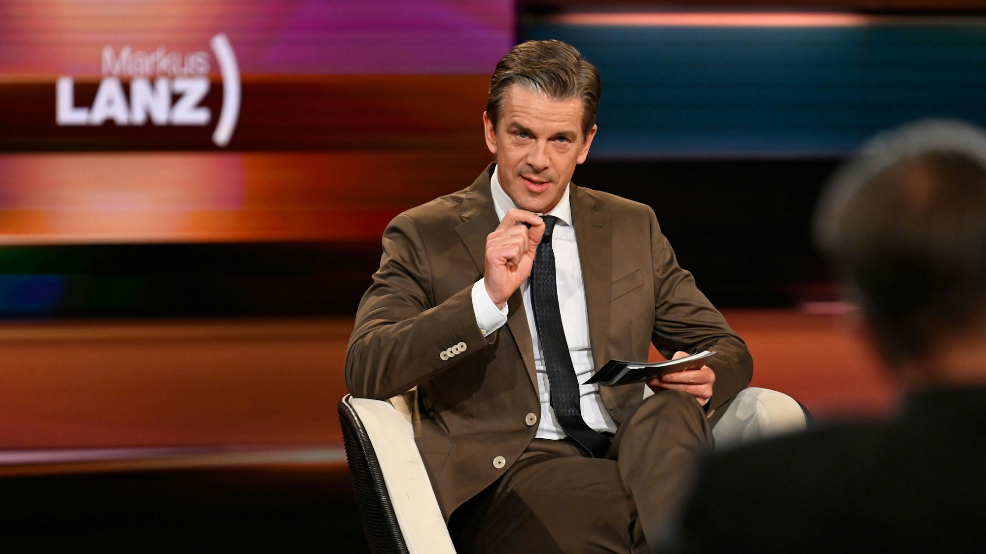 Markus Lanz sitzt bei der Moderation im Studio auf einem Stuhl.