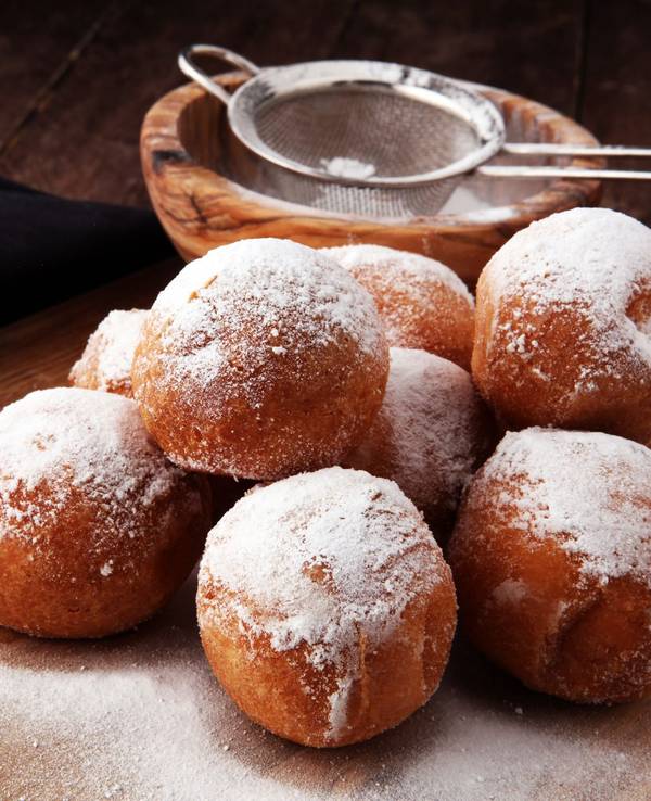 Quarkbällchen, die mit Puderzucker bestäubt sind, liegen auf einem Holztisch