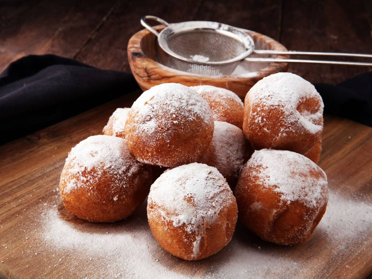 Quarkbällchen, die mit Puderzucker bestäubt sind, liegen auf einem Holztisch