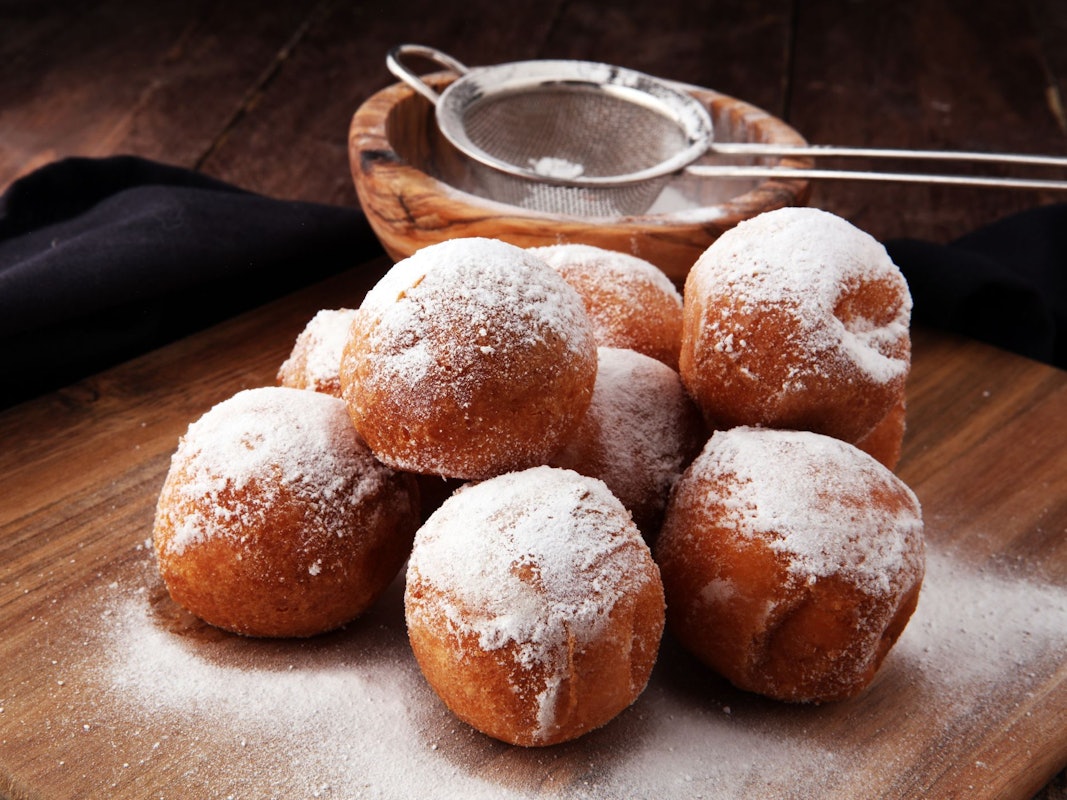 Quarkbällchen, die mit Puderzucker bestäubt sind, liegen auf einem Holztisch