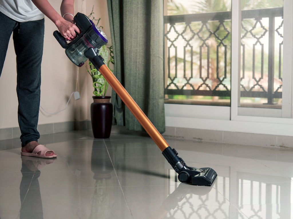 Eine Frau saugt mit einem Akkustaubsauger den Boden.