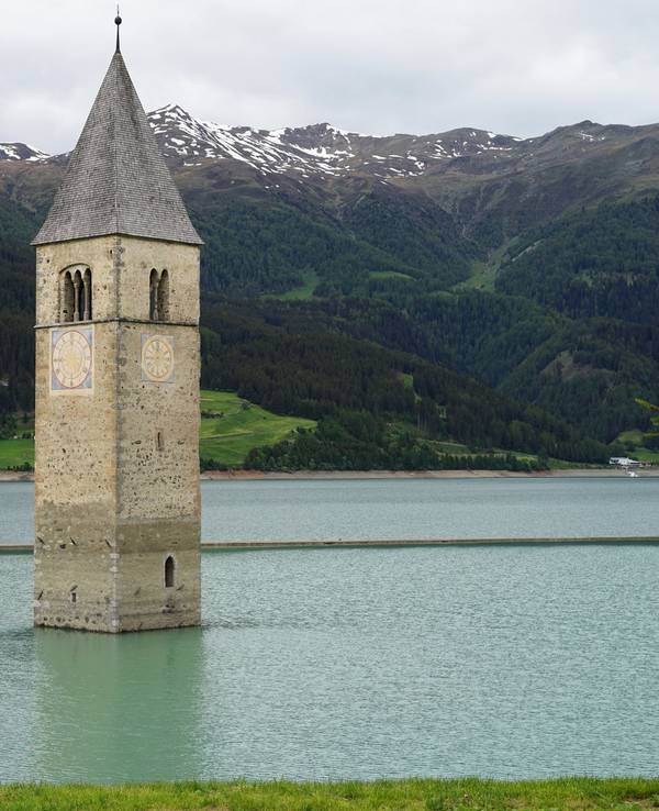Der Kirchturm des alten Dorfes ragt aus dem Reschensee in Südtirol.