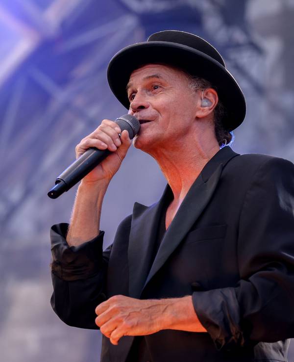 Peter Brings steht mit schwarzem Anzug und schwarzem Hut auf der Bühne und singt in ein Mikrofon.