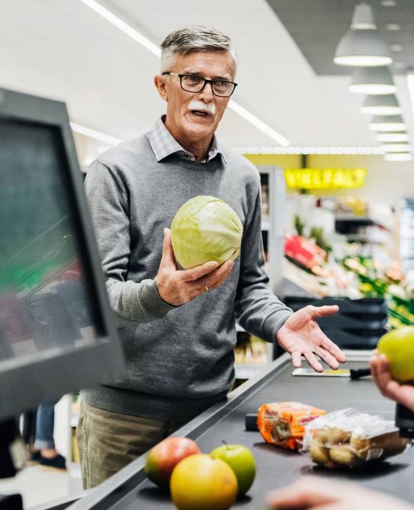 Ein älterer Mann diskutiert an der Kasse mit einer Kassiererin.