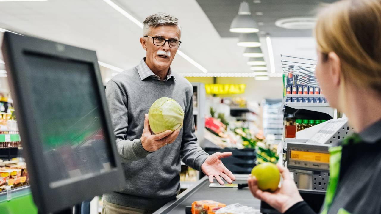 Ein älterer Mann diskutiert an der Kasse mit einer Kassiererin.