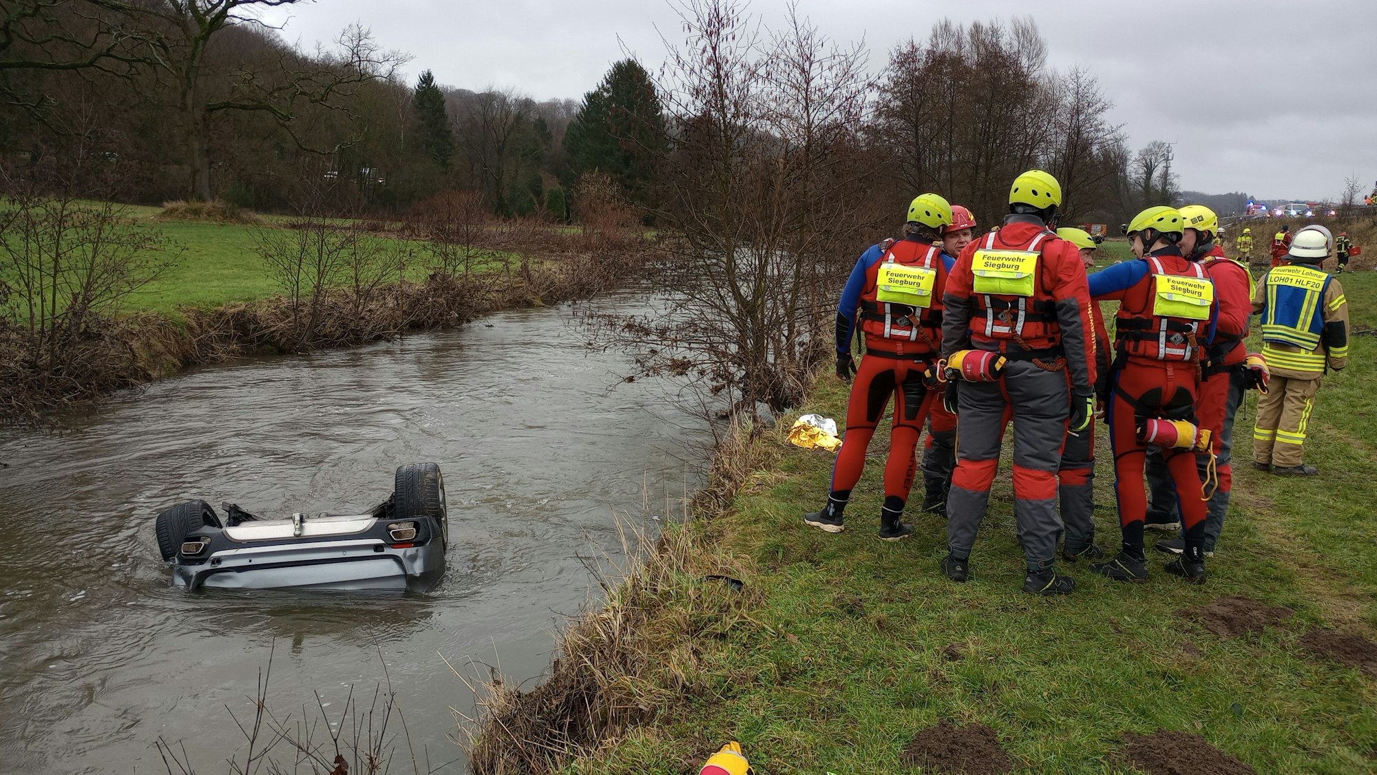 Feuerwehrleute stehen neben einem Auto im Fluss Sülz.