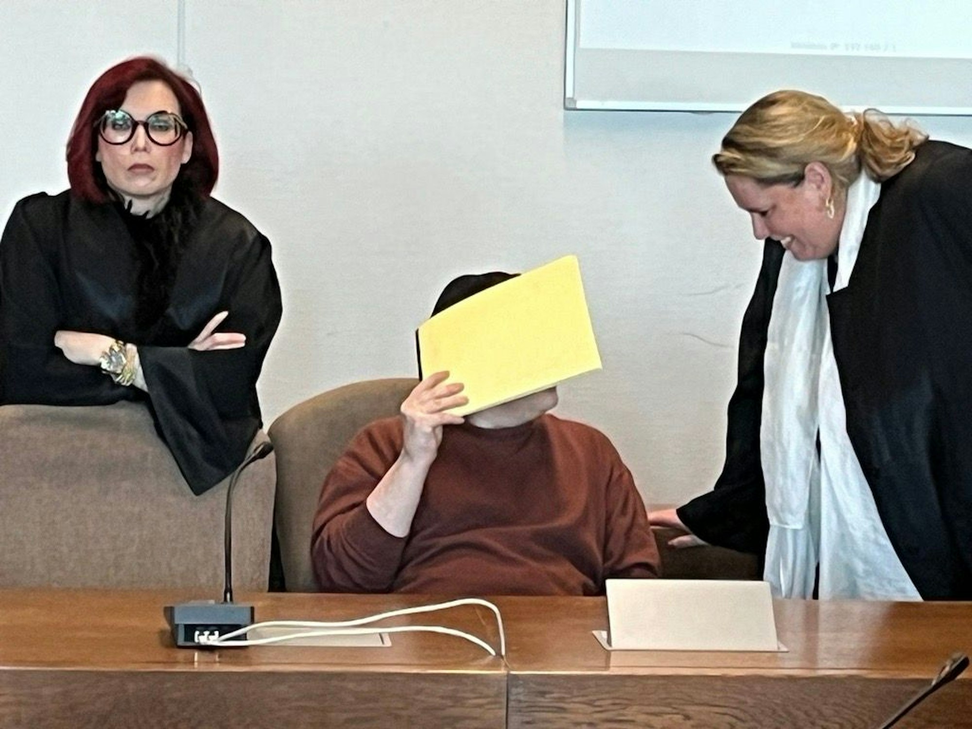 Ein Angeklagter versteckt sich vor den Kameras.