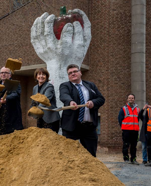 Eine Gruppe von Menschen steht mit Schaufeln vor einem kleinen Hügel Sand.