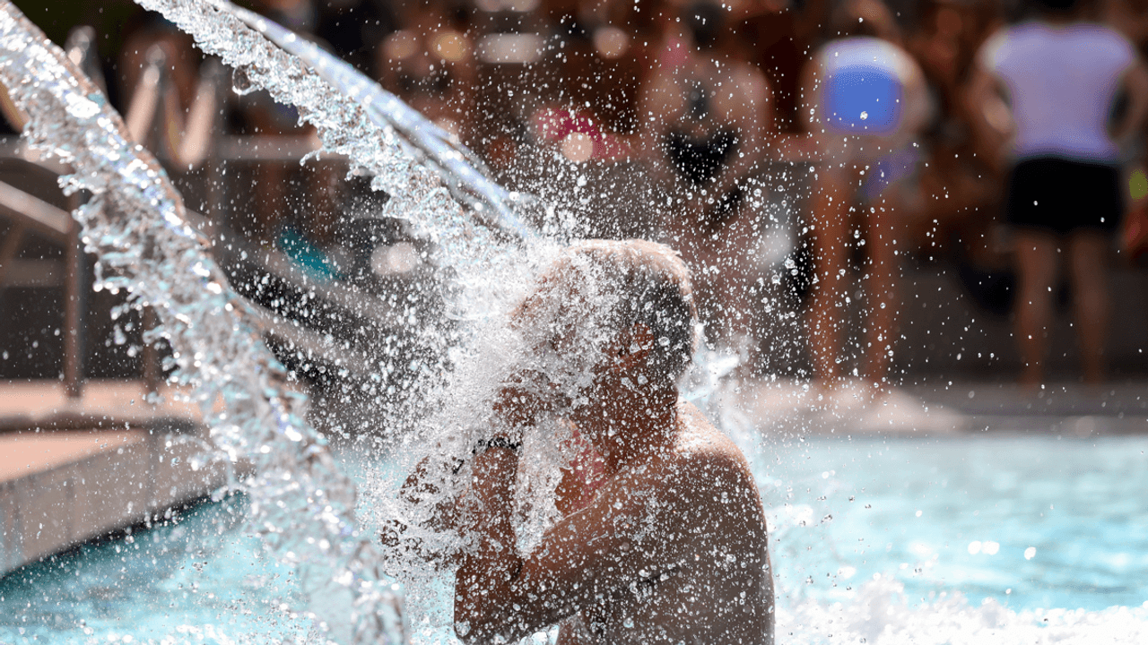 Ein Mann erfrischt sich im Pool unter einer Wasserfontäne.