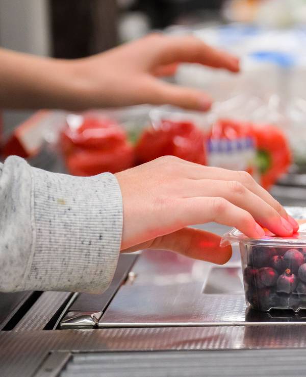 Eine Kassiererin scannt Heidelbeeren an der Kasse eines Supermarktes.