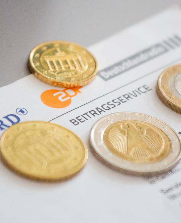 Euromünzen liegen auf einem Anschreiben zur Anmeldung für die Rundfunkgebühren, neben den Logo von ARD (l-r), ZDF und Deutschlandfunk.