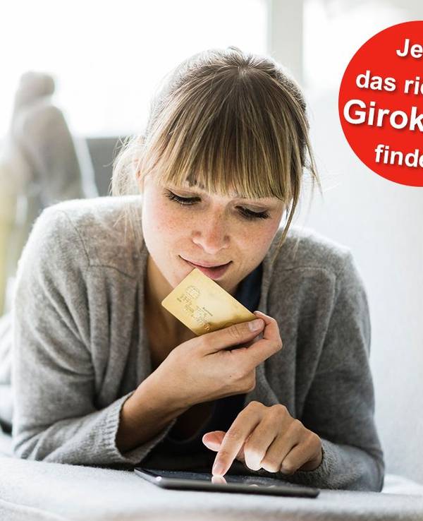 Eine Frau liegt auf dem Sofa und hält eine Bankkarte in der Hand während sie auf ihrem Tablet etwas eingibt.