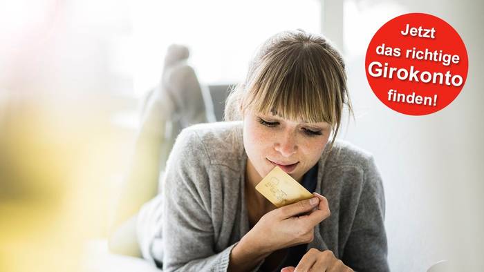 Eine Frau liegt auf dem Sofa und hält eine Bankkarte in der Hand während sie auf ihrem Tablet etwas eingibt.