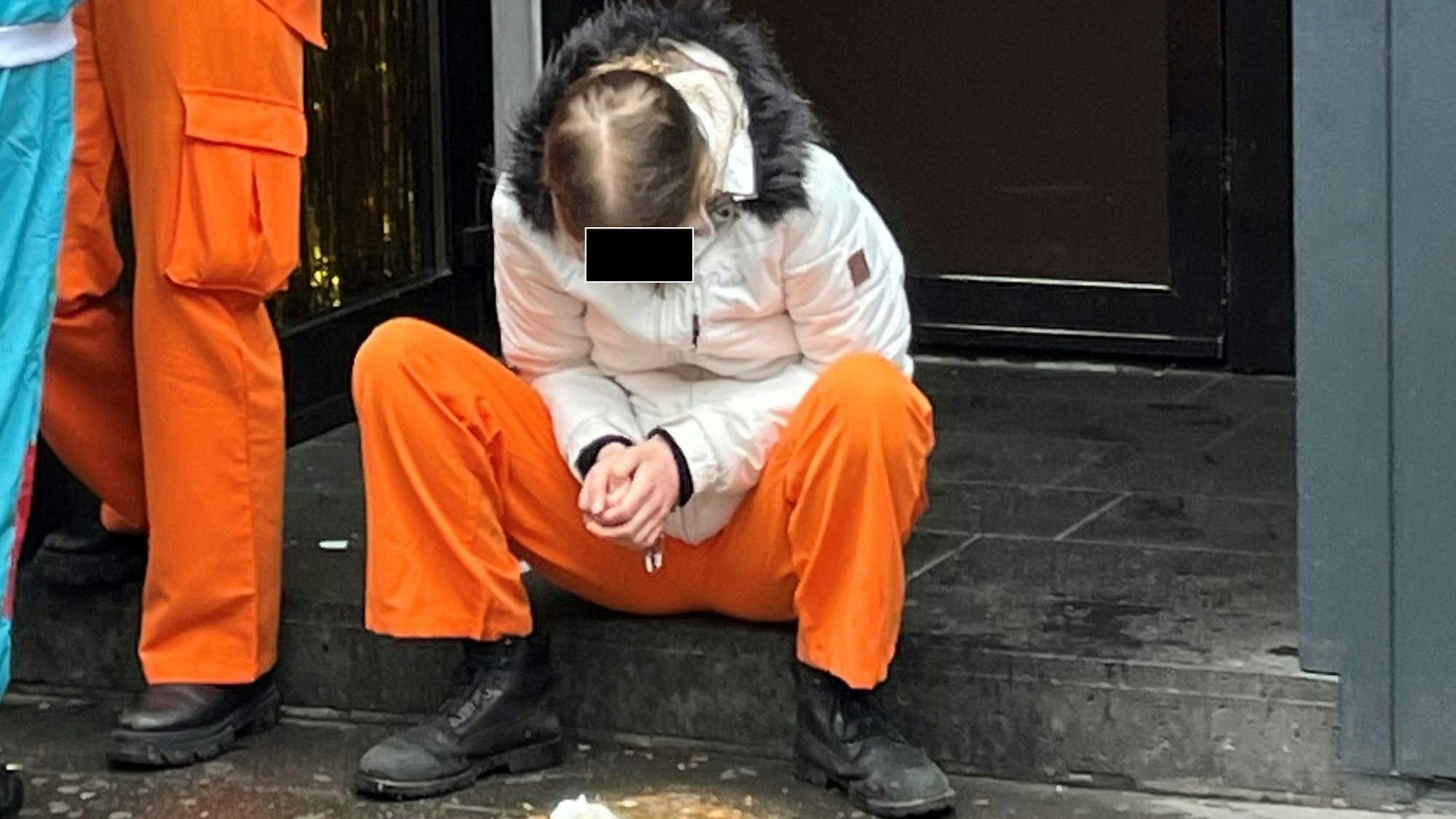 Eine junge Person sitzt auf der Stufe eines Hauseingangs und hat sich erbrochen.