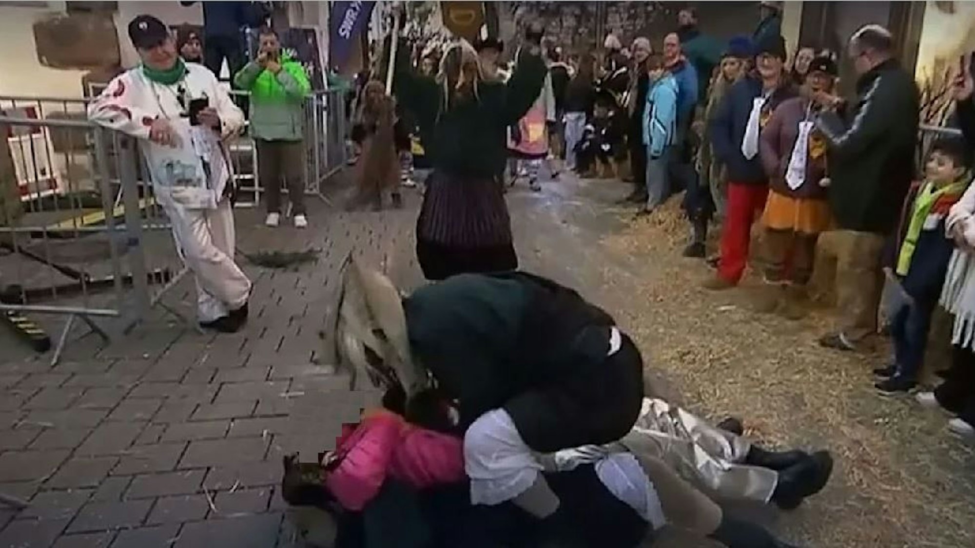 Ein als Hexe verkleideter Mann simuliert sexuelle Handlungen an einer am Boden liegenden Reporterin.