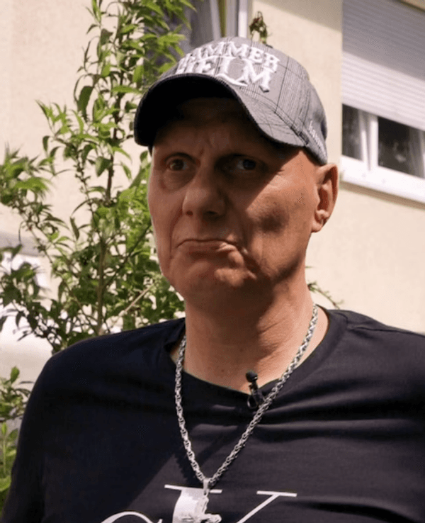 Elvis trägt eine Kappe und eine silberne Kette. Er blickt in die Kamera.