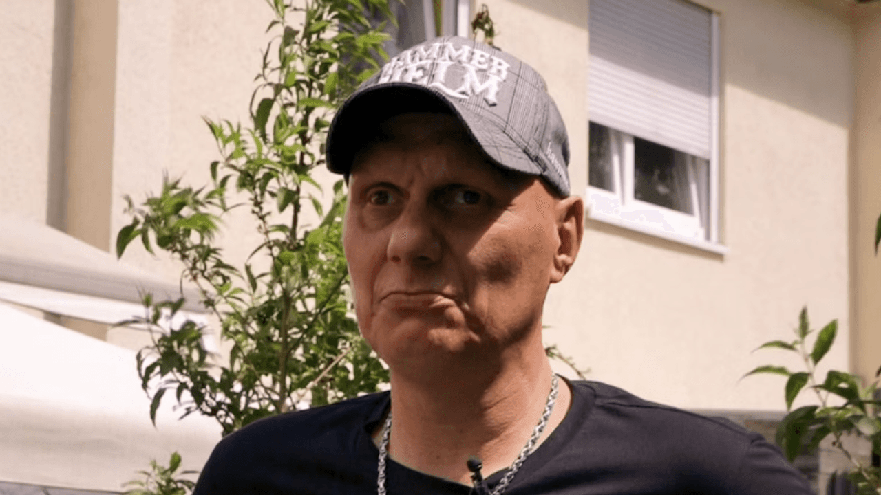 Elvis trägt eine Kappe und eine silberne Kette. Er blickt in die Kamera.