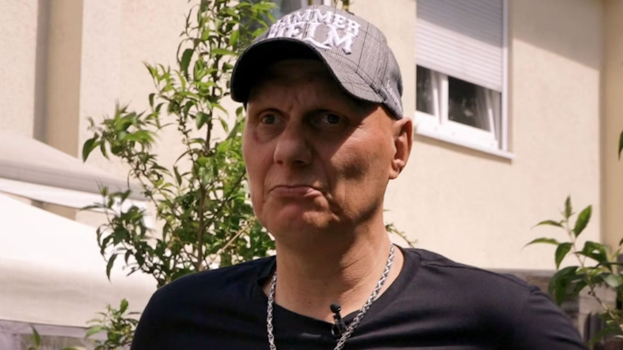 Elvis trägt eine Kappe und eine silberne Kette. Er blickt in die Kamera.