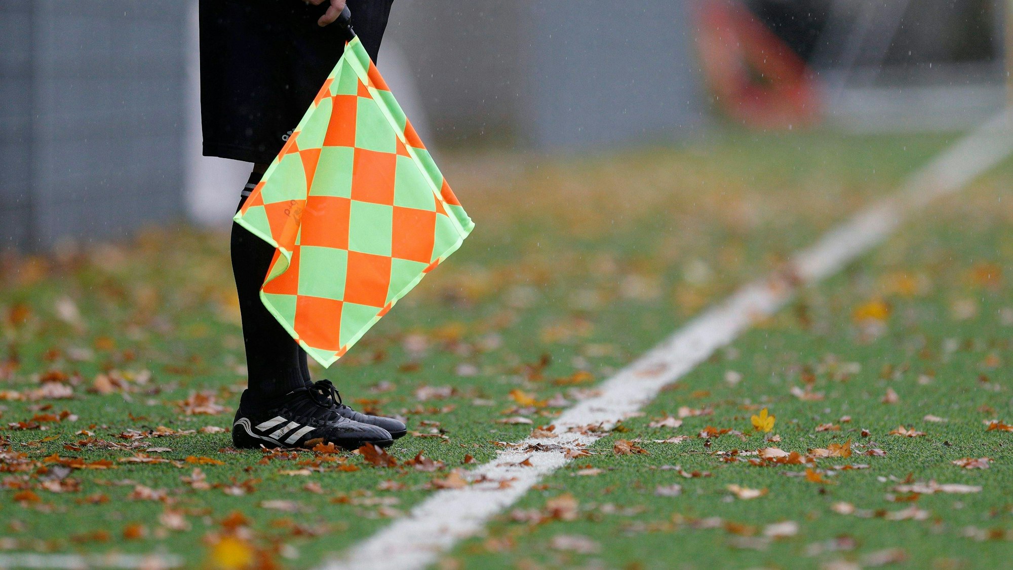 Die Beine eines Linienrichters, der mit Fahne an der Seitenlinie steht,