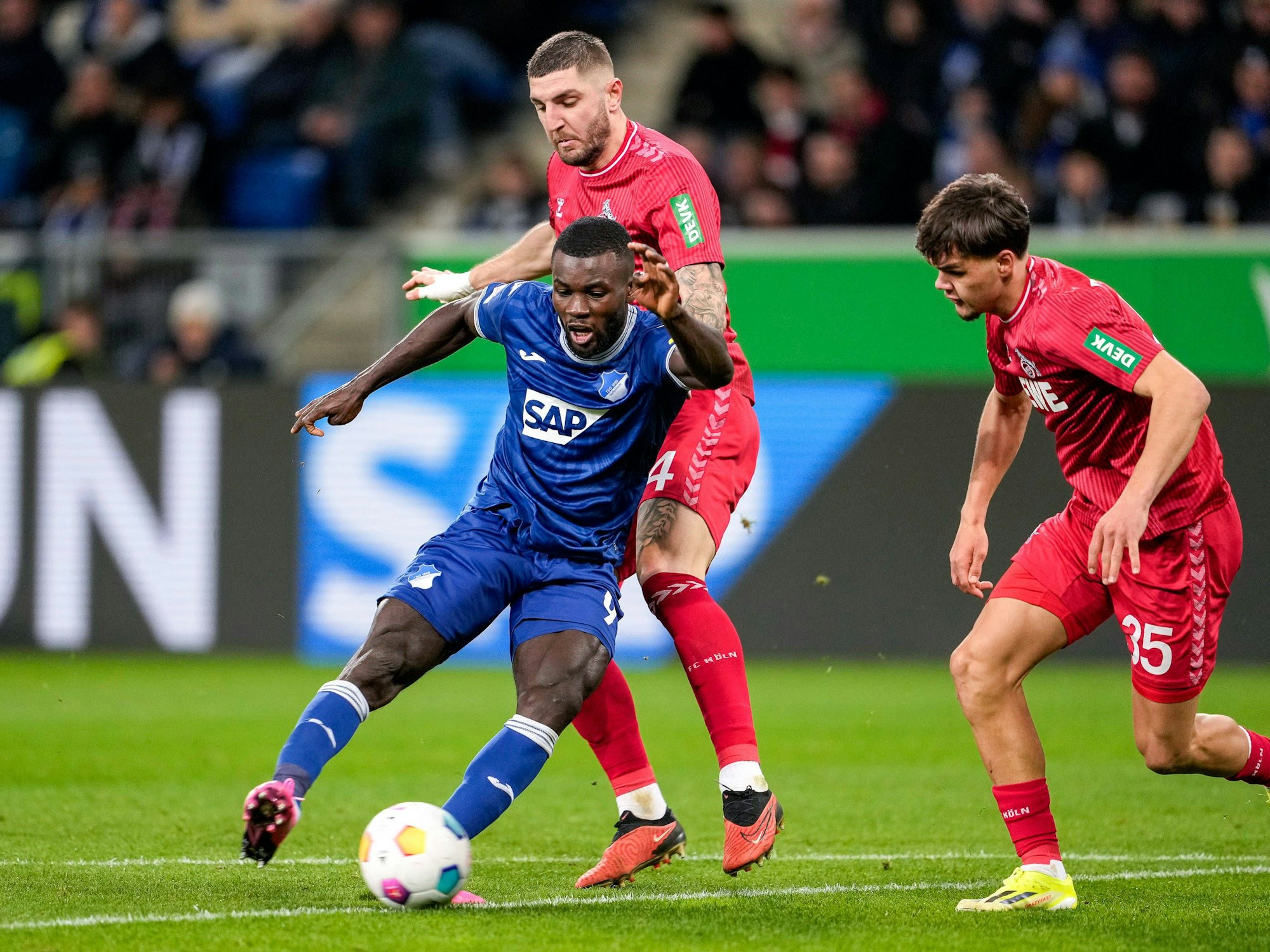Ihlas Bebou (Hoffenheim) schießt, Kölns Jeff Chabot und Max Finkgräfe versuchen zu stören.