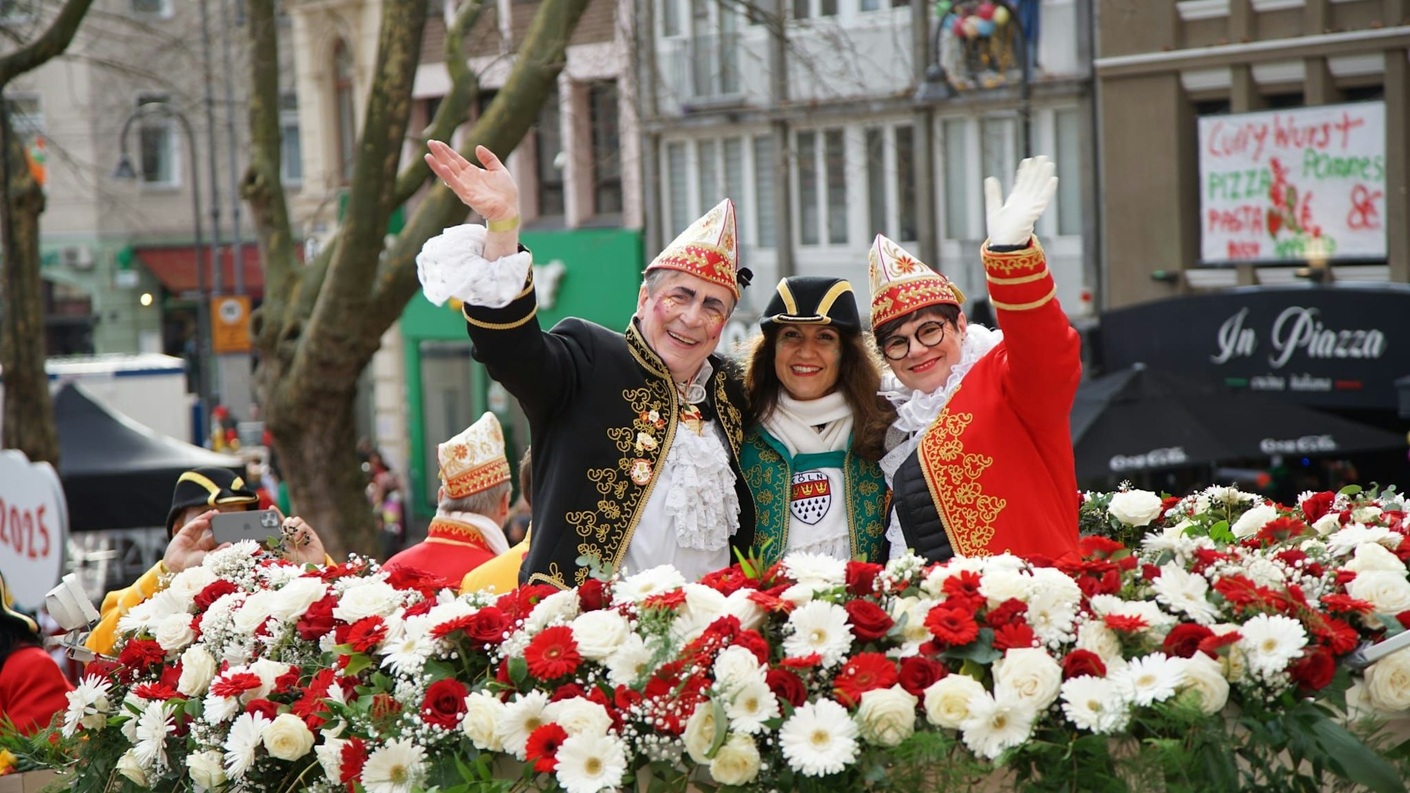 Ein Mann und zwei Frauen winken vom Wagen in die Kamera.