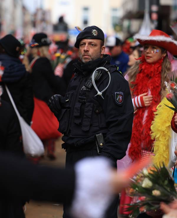 Ein Polizist steht inmitten von Karnevalistinnen und Karnevalisten im Rosenmontagsumzug.