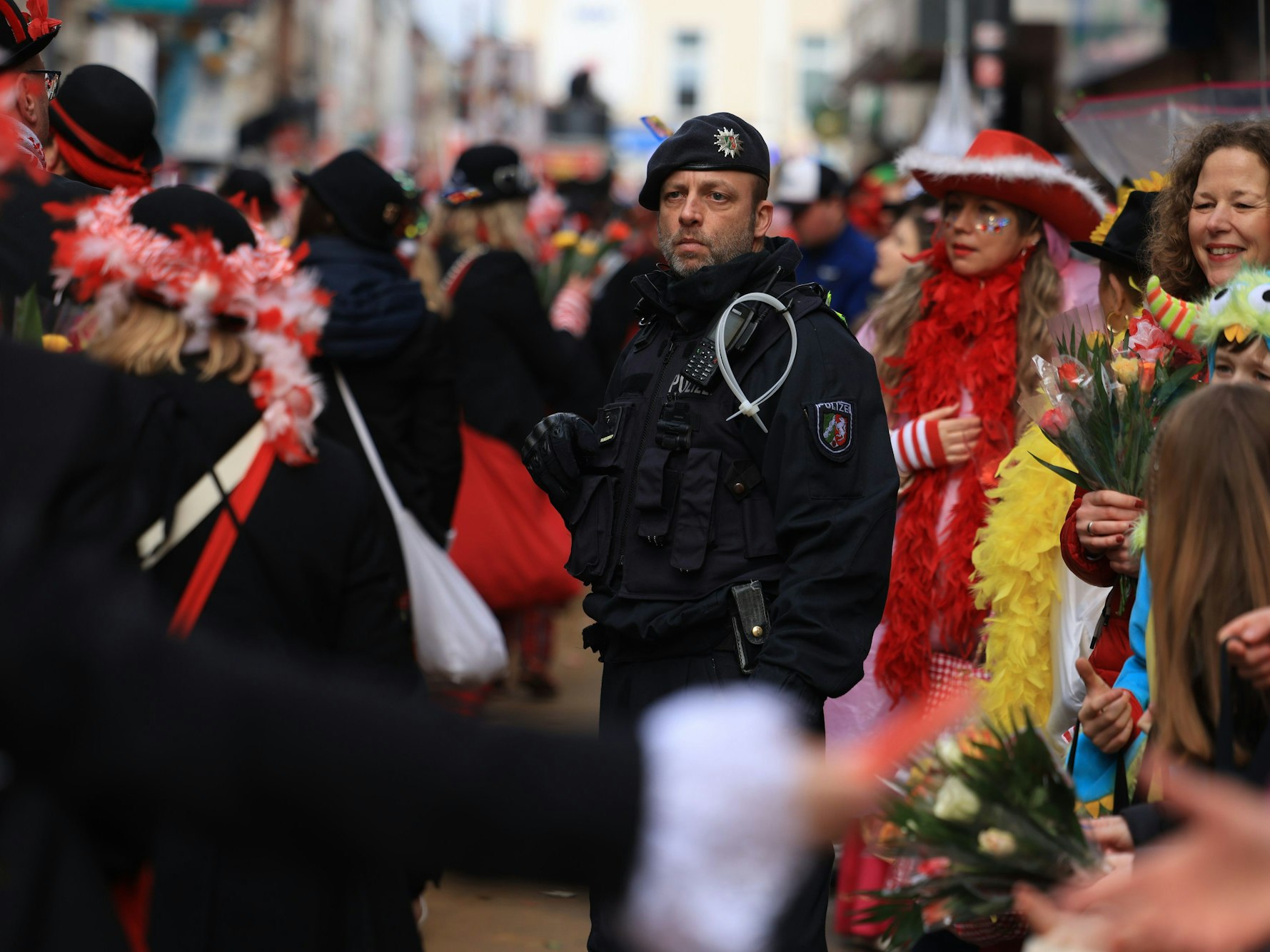 Ein Polizist steht inmitten von Karnevalistinnen und Karnevalisten im Rosenmontagsumzug.