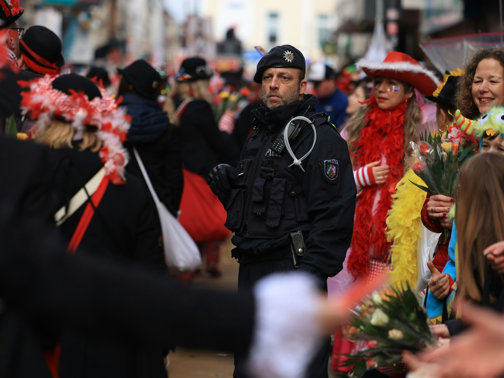 Ein Polizist steht inmitten von Karnevalistinnen und Karnevalisten im Rosenmontagsumzug.