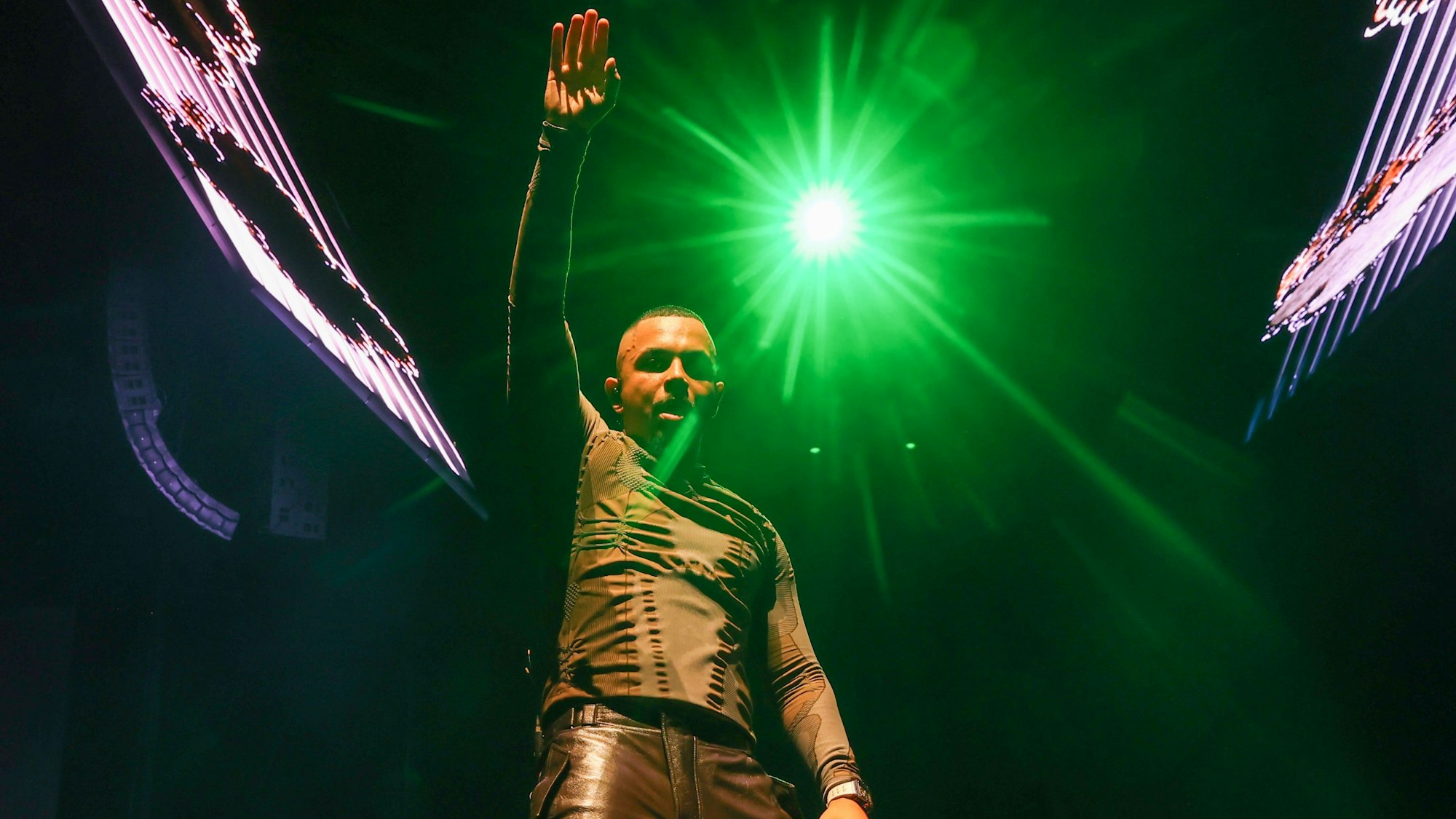 Ein Mann reckt den linken Arm in die Luft und guckt in die Kamera.