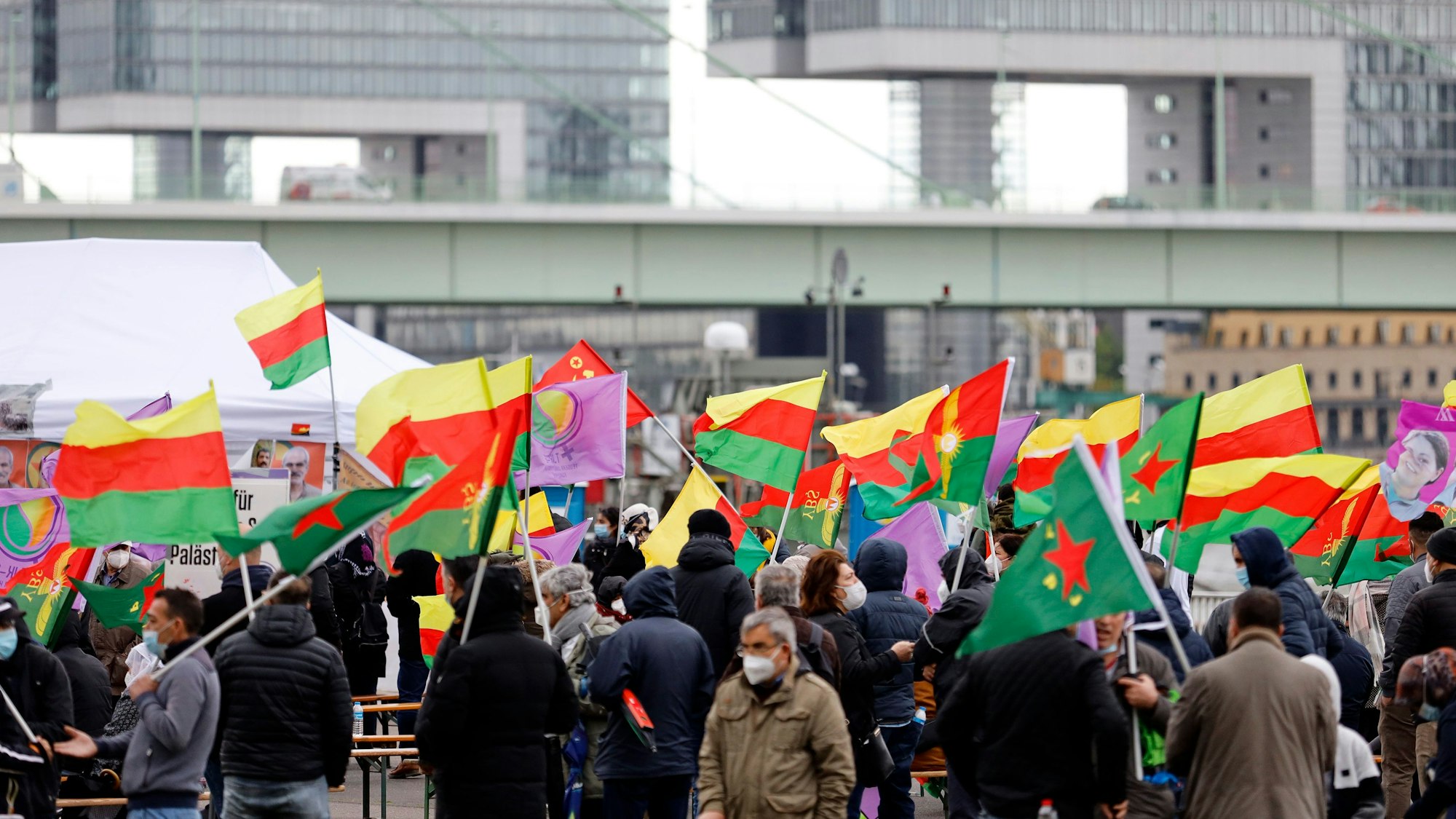 Demonstrierende halten Fahnen hoch, im Hintergrund zwei der Kölner Kranhäuser.