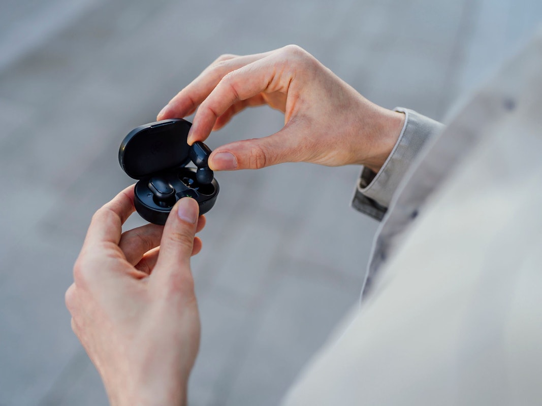 Ein Mann holt schwarze In-Ear-Kopfhörer aus ihrer Ladebox.