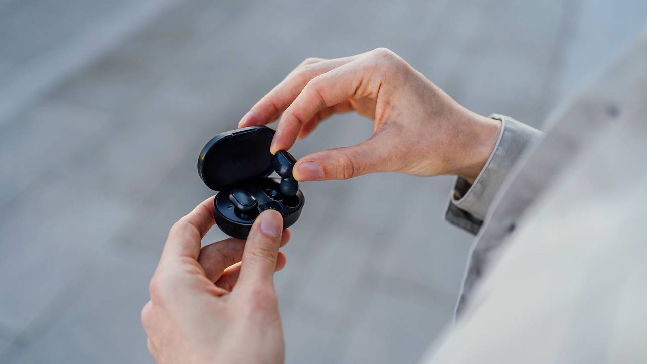 Ein Mann holt schwarze In-Ear-Kopfhörer aus ihrer Ladebox.
