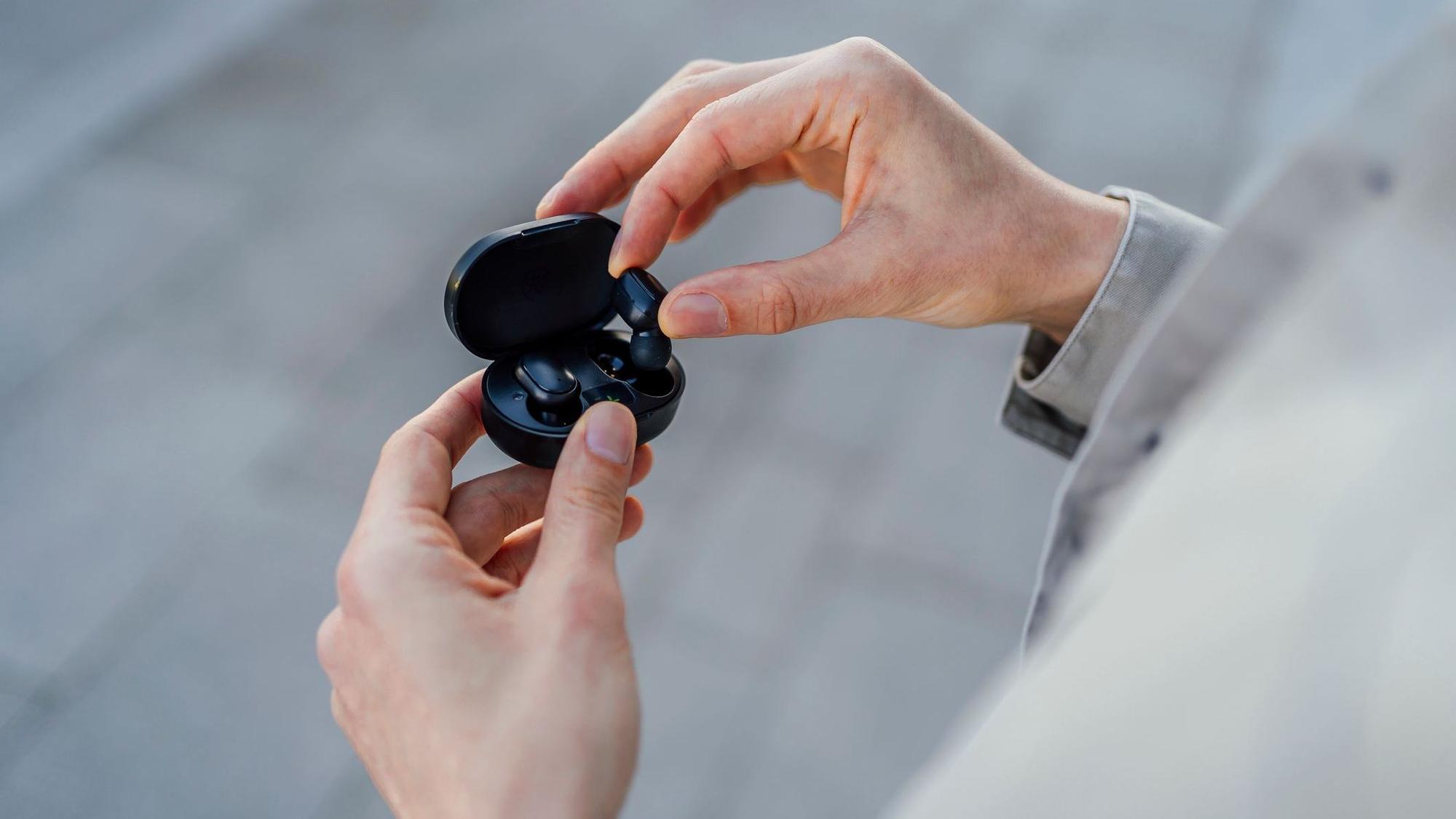 Ein Mann holt schwarze In-Ear-Kopfhörer aus ihrer Ladebox.