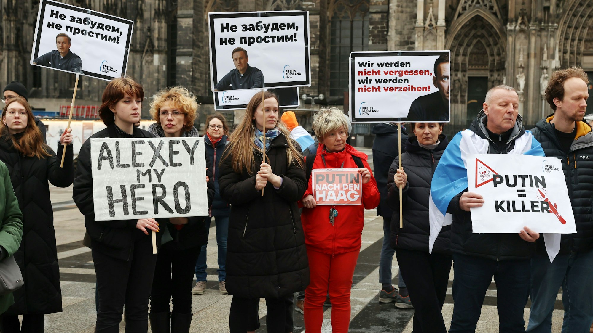 Menschen stehen mit Plakaten vor dem Kölner Dom und gedenken des verstorbenen Alexej Nawalny.