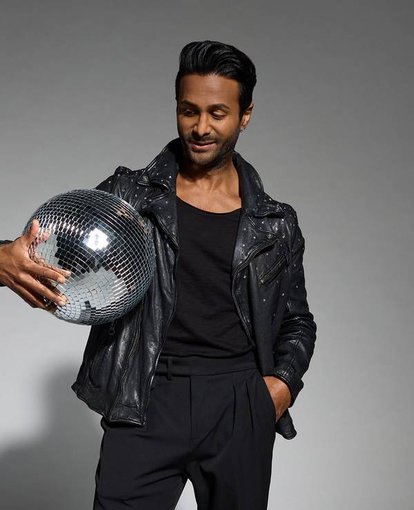 Biyon Kattilathu posiert für die Kamera. Er trägt eine schwarze Hose und eine schwarze Lederjacke, im Arm hält er eine Diskokugel.