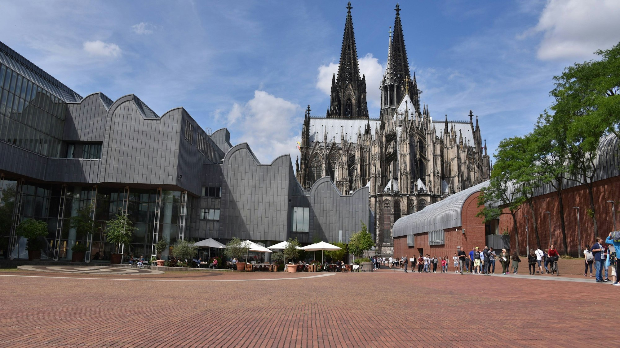 Der Heinrich-Böll-Platz bei strahlendem Sonnenschein, im Hintergrund sieht man den Dom.