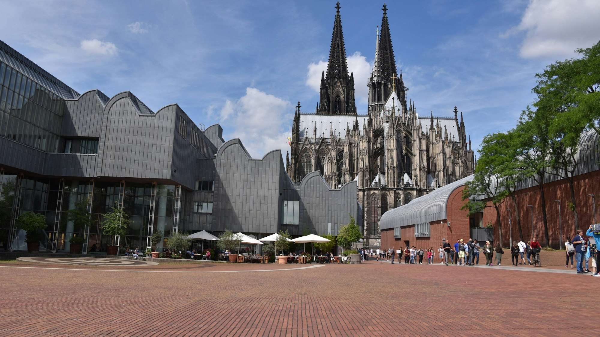 Der Heinrich-Böll-Platz bei strahlendem Sonnenschein, im Hintergrund sieht man den Dom.