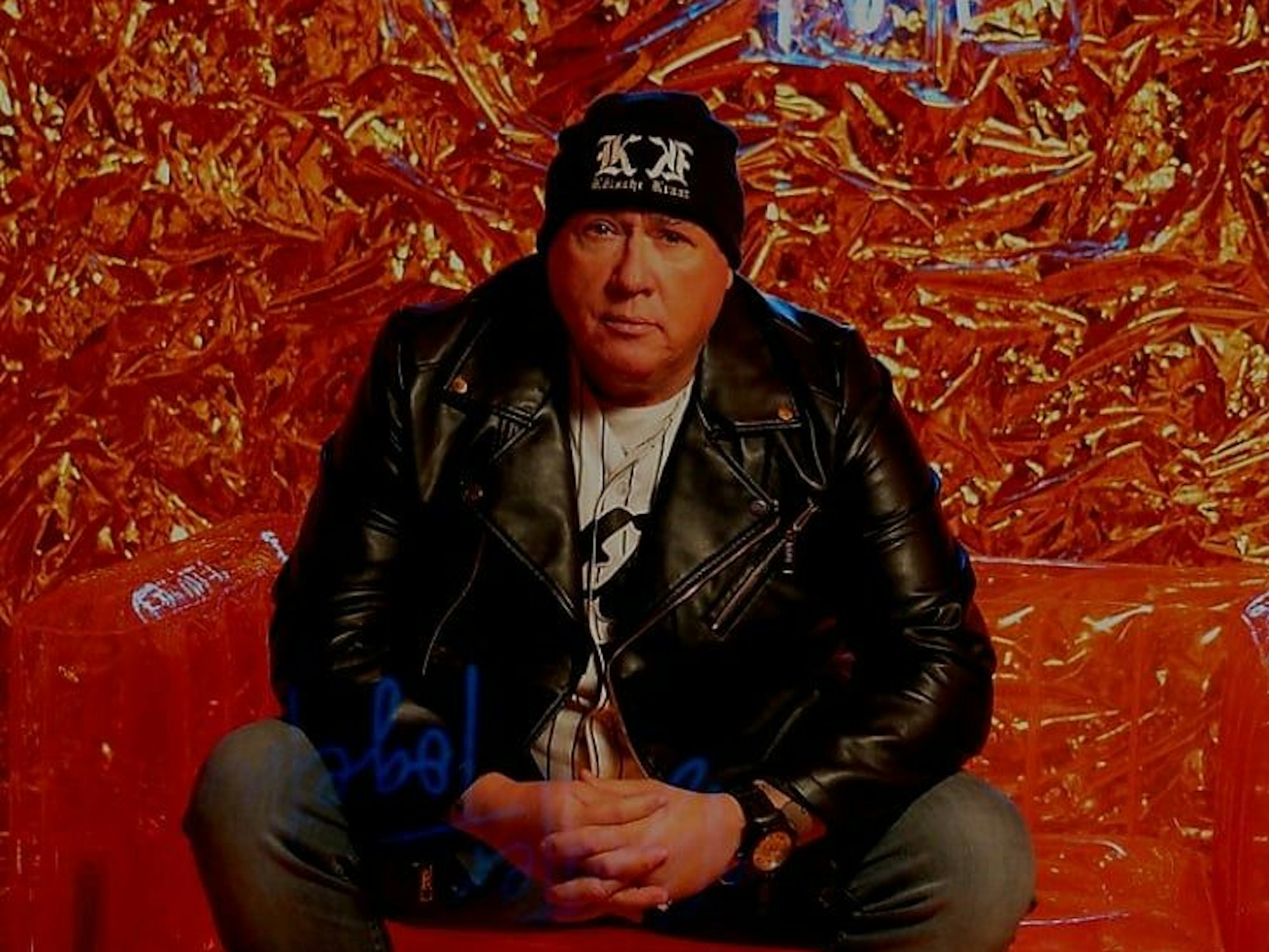 Ramon Ademes sitzt auf einem Stuhl vor rotem Hintergrund.