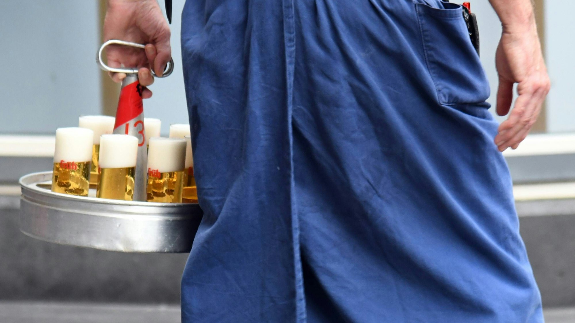 Ein Köbes serviert in einem Kölner Brauhaus auf der Domplatte Kölsch in den typischen Kölschglässern.