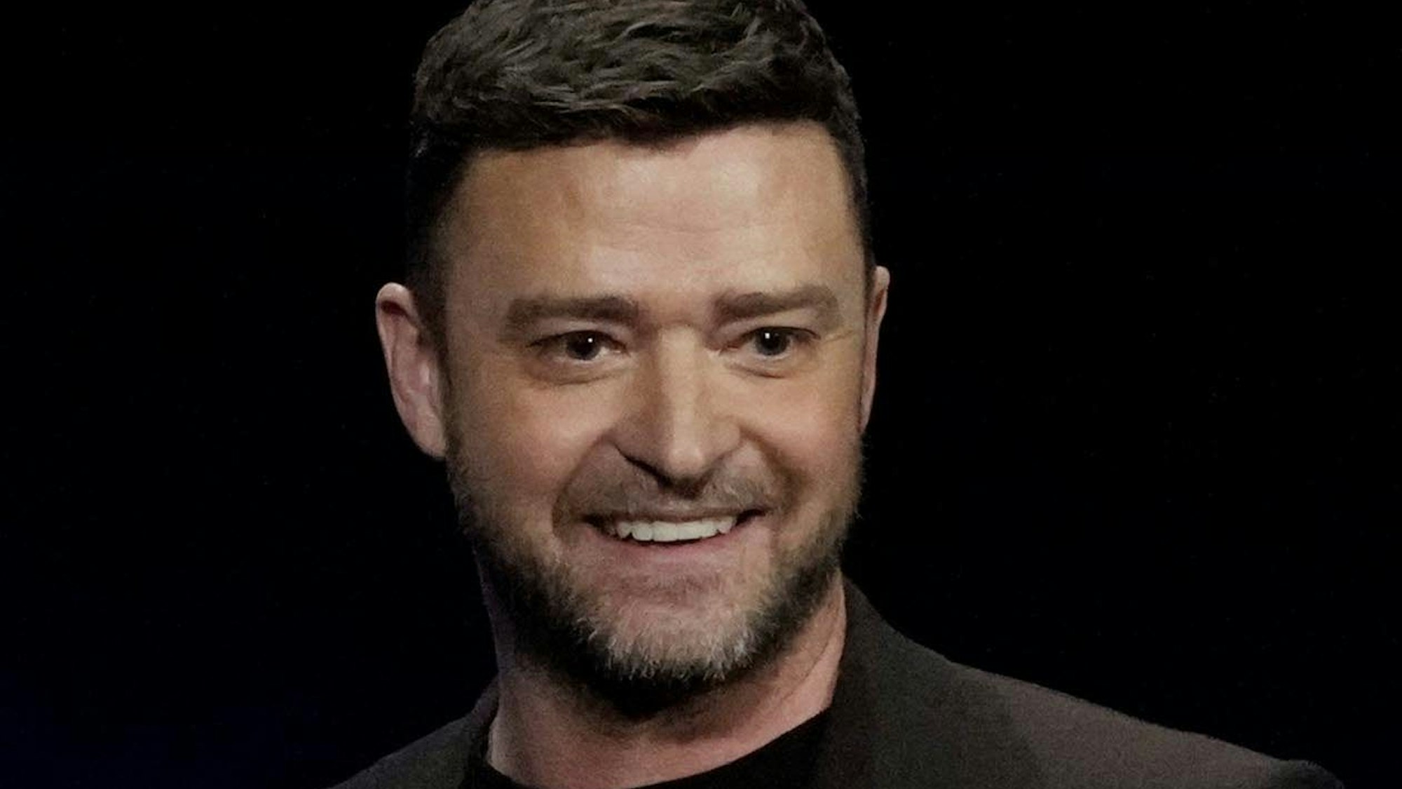 Justin Timberlake in schwarzen Klamotten auf einer Bühne, er lächelt.