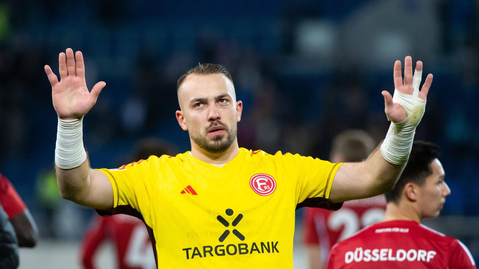 Fortuna Düsseldorfs Torwart Florian Kastenmeier hebt vor der Fankurve entschuldigend die Arme.